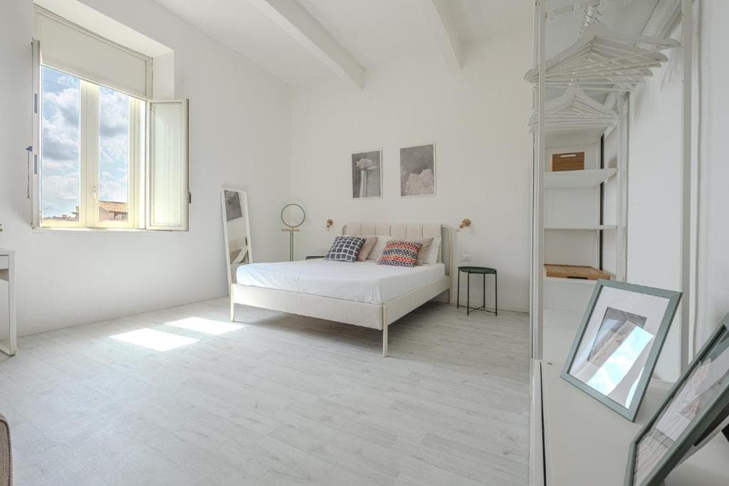 The bright double bedroom, white iron bed beneath the beamed ceiling and morning light across the pale floor