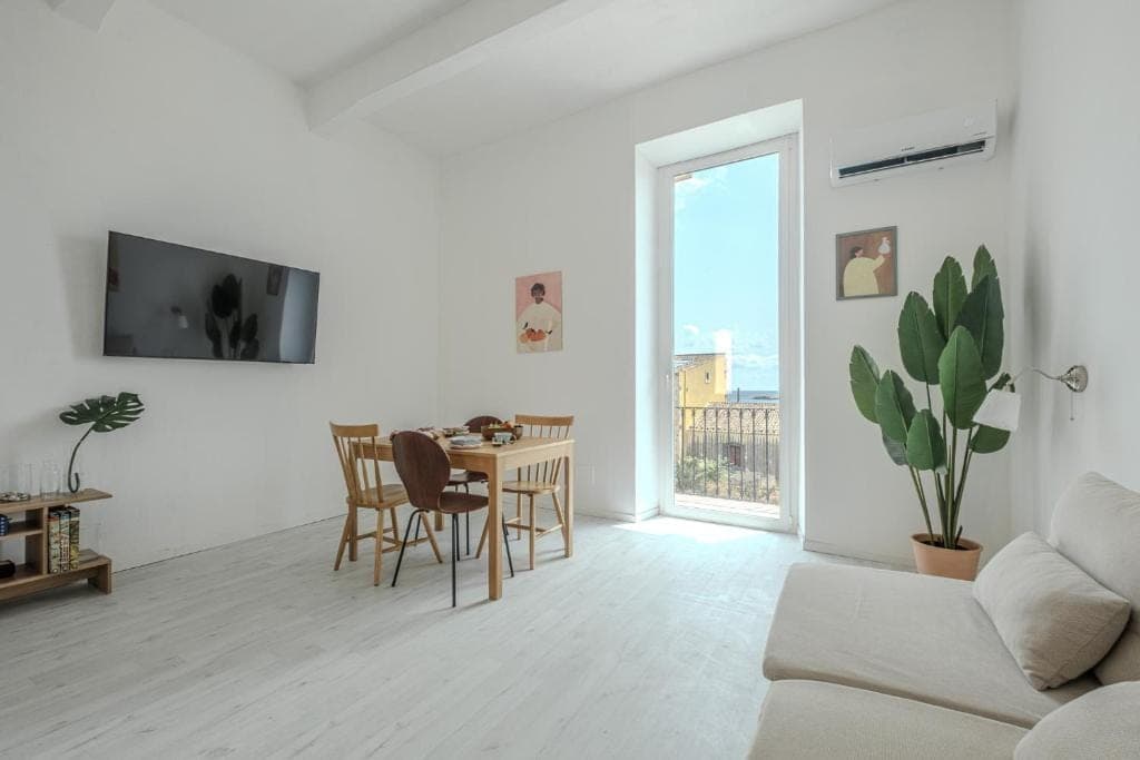 The dining area with the balcony door open and a tall plant beside the sofa